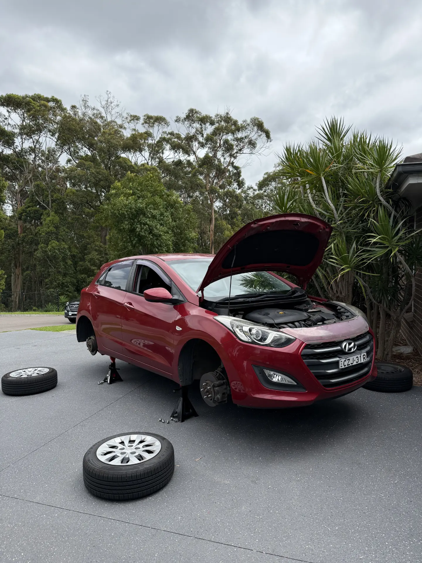Red Hyundai i30 hatch raised on jack stands with wheels removed and bonnet up during a mobile mechanic call-out - Meek Mobile, Newcastle